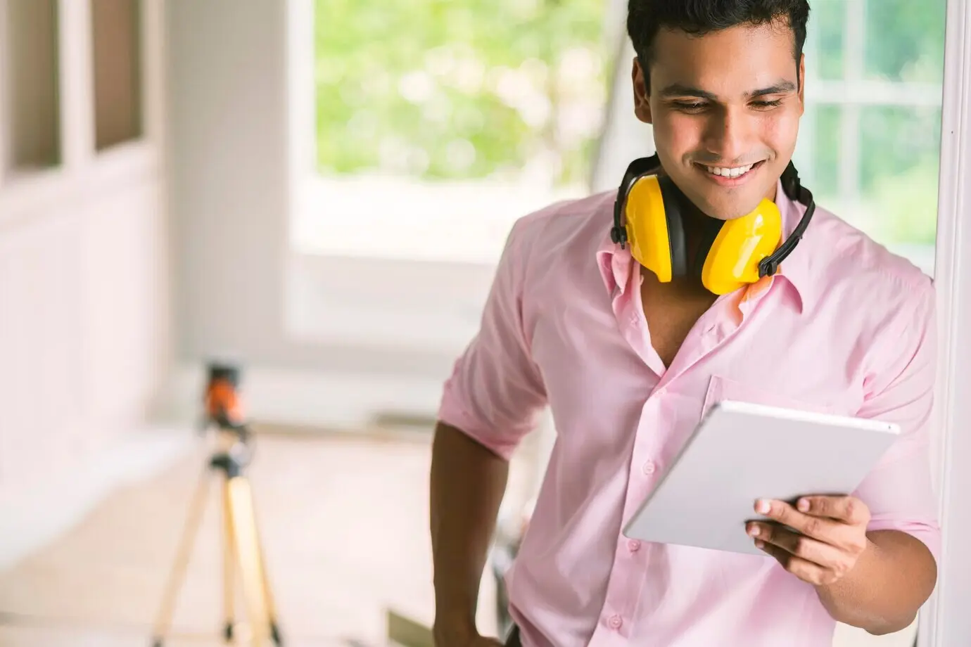 Smarter indischer Schreiner-Auftragnehmer mit Schutzbrille und Kopfhörer überprüft eine weiße Deckenleiste für ein Konzept der Innendekoration eines Hauses.